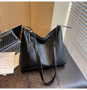Détail d'un grand sac cabas noir en similicuir avec bandoulière large et étiquette