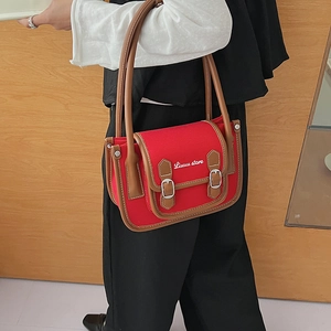 Détail du sac bandoulière en toile rouge avec bordure en cuir marron et broderie chic