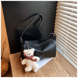 Close-up of black lychee grain leather pillow bag with a cute teddy bear charm