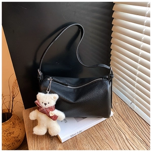 Detail of black pebble leather shoulder bag with a cute plush bear charm on a wood table