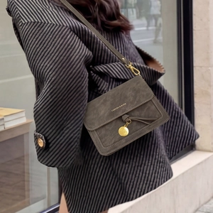 Detail of dark grey flap crossbody bag with gold tassel and metal pendant on model