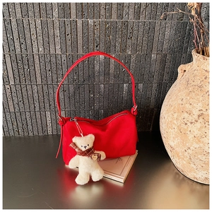 Detail of red shoulder bag with metallic zipper and a cute white teddy bear plush charm