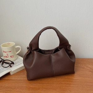 Close-up of deep brown lychee leather handbag with pleated details on a wooden table