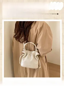 Detail of a beige bucket bag featuring a drawstring closure and circular top handle