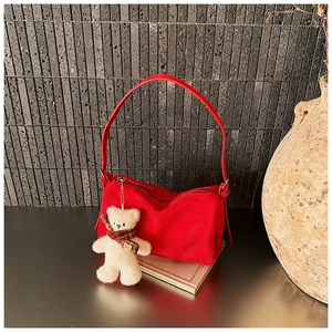 Detail of red suede pillow bag featuring a cute white plush bear charm and zip closure