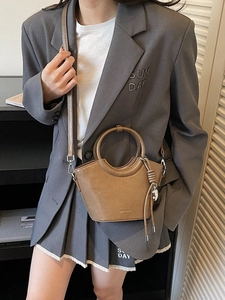 Sac seau en cuir marron avec poignées anneaux et pompon porté par un mannequin