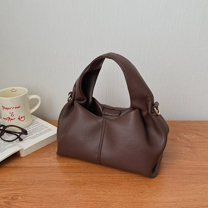 Detail of deep brown dumpling bag showing twisted handle and litchi grain leather texture