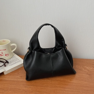 Detailed view of black lychee grain leather handbag with natural folded design on wooden table