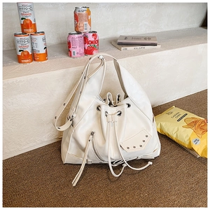 Detail of cream drawstring bucket bag featuring silver rivets and side zipper accents