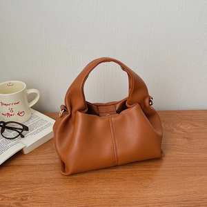 Detailed view of caramel faux leather pleated cloud bag on a rustic wooden table top