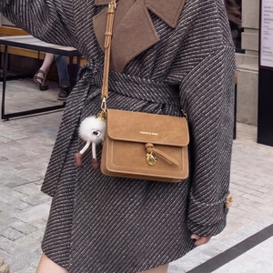 Detail of brown suede crossbody bag with contrast stitching and fuzzy plush doll charm