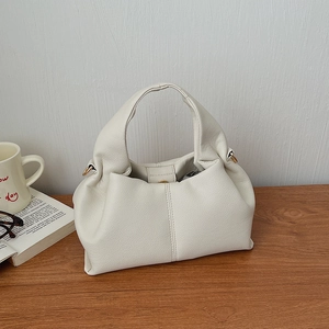 Detail view of cream leather cloud handbag featuring lychee texture and magnetic buckle