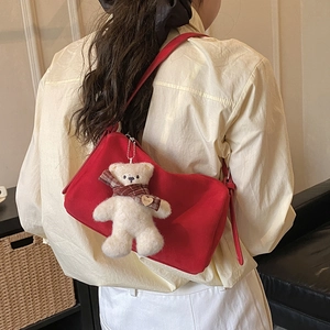Macro detail of red suede shoulder bag with a cute plush bear charm and heart detail