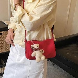 Close-up of a red suede pillow bag with a plush bear charm on a black sofa