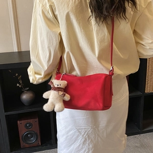 Detail view of red suede pillow bag with a cute teddy bear charm on model back
