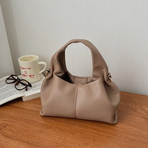 Detail view of brown pebbled leather cloud bag showing soft pleats and metal ring accents