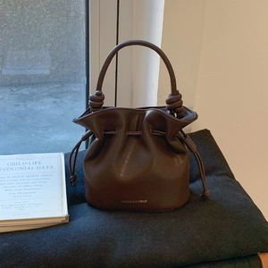 Detail of dark brown leather bucket bag showing knot handle and gold logo print