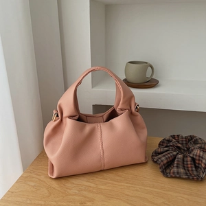 Detail of dusty rose cloud handbag on wooden table with elegant pleats and gold ring