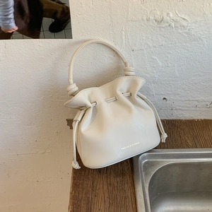 Detailed close-up of cream leather bucket bag showing drawstring closure and brand logo