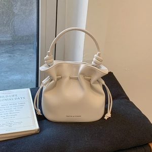 Detail view of cream bucket bag showing knotted handle and branded lettering on fine leather