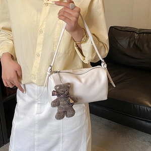 Close-up of cream pillow bag with lychee texture and cute plush bear charm detail