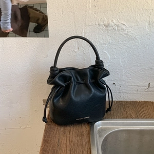 Detail view of black matte leather bucket bag featuring drawstring closure and gold brand logo