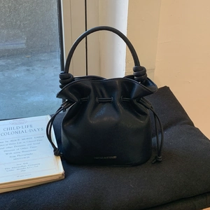 Detail of minimalist black leather bucket bag showing drawstring closure and knotted handle