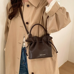 Detail of dark brown drawstring bucket bag with white printed text and leather texture