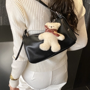 Close-up of black lychee leather pillow bag with a cute plush bear charm on white sweater
