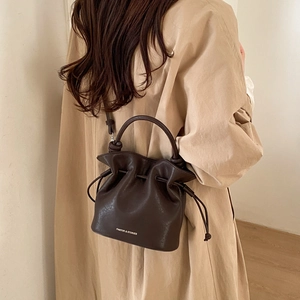 Detail of a dark brown leather bucket bag with drawstring closure and crossbody strap