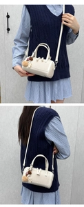 Detail of a beige cylinder boston bag with plush bear charm and detachable strap