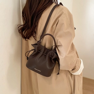 Detail of a dark brown leather bucket bag with white logo and drawstring closure