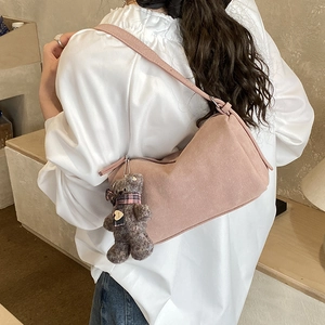 Detail view of pink suede shoulder bag with cute plush bear charm on a model's back