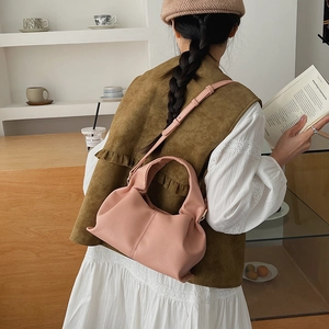 Pink pleated dumpling bag with adjustable strap shown in a lifestyle indoor setting