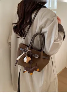 Braune Leder-Eimertasche mit Hundeanhänger und Baseball-Deko auf beigem Trenchcoat