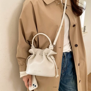 Model wearing a cream drawstring bucket bag with handle and shoulder strap details