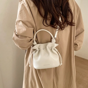 Detailed view of white bucket bag with drawstring closure worn by model in trench coat