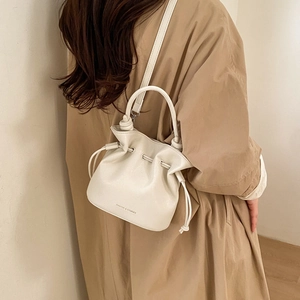 Detailed side view of beige leather bucket bag with drawstring and knot detail on a model