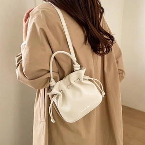 Minimalist beige drawstring bucket bag with knot handle detail worn with a trench coat
