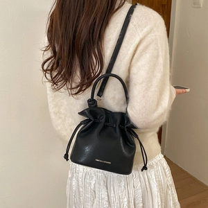 Detail of black drawstring bucket bag showing textured leather and brand logo engraving