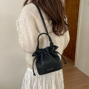 Black drawstring bucket bag shown on a model in a minimalist modern interior setting