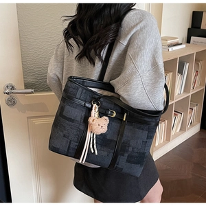 Detalle del bolso tote tejido azul con correas de cuero negro y colgante de oso de peluche