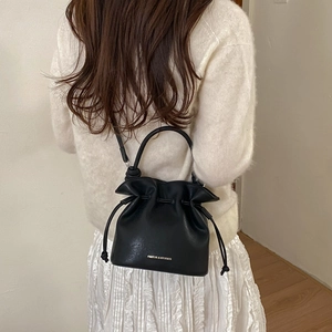 Detail of a minimalist black leather drawstring bucket bag worn by a model in a casual setting
