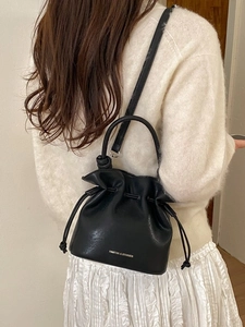 Minimalist black drawstring bucket bag with handle and shoulder strap worn by a model