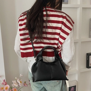 Detail of black leather cloud bag worn as a shoulder bag against a minimalist background
