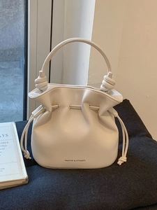 Minimalist white leather bucket bag with drawstring closure and knotted handle details