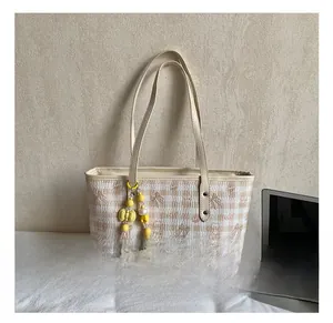 Close-up of beige plaid tote bag with cream leather straps and yellow beaded bow charm