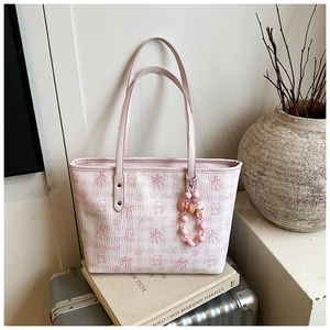 Detail of pink tote bag with bear print and beaded charm on a silver suitcase