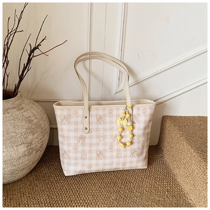Close-up of cream plaid tote bag with pink bow and bear prints on a woven mat