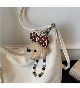 Macro detail of plush teddy dog bag charm with polka dot bow and beaded chain